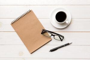 Modern office desk table with notebook and other supplies with cup of coffee. Blank notebook page for you design. Top view, flat lay photo