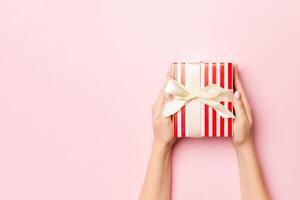 Female's hands holding striped gift box with colored ribbon on living coral background. Christmas concept or other holiday handmade present box, concept top view with copy space photo