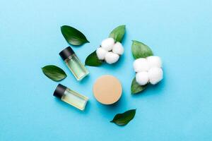 Organic cosmetic products with cotton flower and green leaves on color background. Flat lay photo