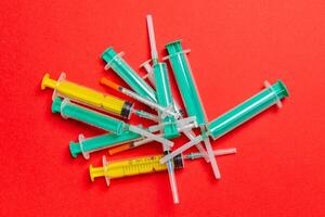 Top view of a pile of medical syringes and insulin syringes with needles at red background with copy space. Injection treatment concept photo