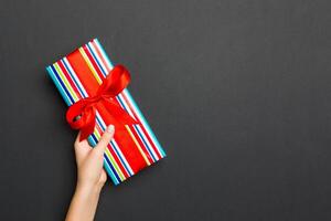 Top view of female hands holding christmas or other holiday handmade present box package in the palms, flat lay on black background with copy space photo