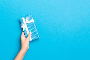 Woman arms holding gift box with colored ribbon on blue table background, top view and copy space for you design photo