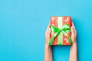 Woman arms holding gift box with colored ribbon on blue table background, top view and copy space for you design photo