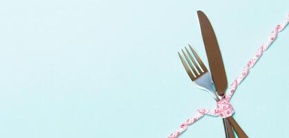 dieta y concepto de alimentación saludable con tenedor y cuchillo cruzados y cinta métrica rizada sobre fondo azul. vista superior de pérdida de peso con espacio de copia foto