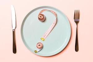 Question mark made of measuring tape on round plate on pink background. Top view of hesitation and diet concept photo