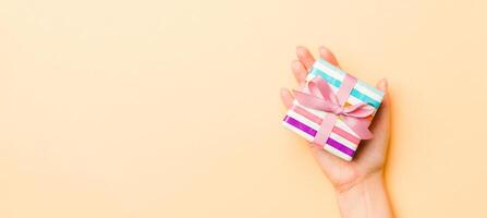 Flat lay of woman hands holding gift wrapped and decorated with bow on gold background with copy space. Christmas and holiday concept photo