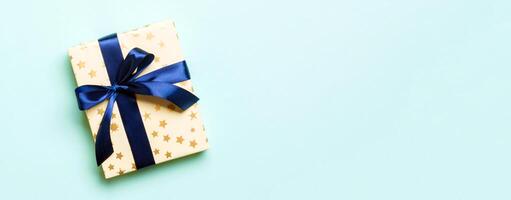 Top view woman hands holding Christmas present box with blue bow on blue background with copy space photo