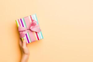 Flat lay of woman hands holding gift wrapped and decorated with bow on gold background with copy space. Christmas and holiday concept photo