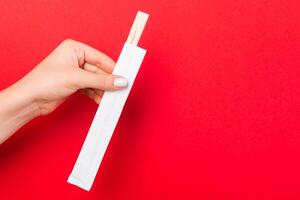 Cropped image of hand giving chopsticks on red background. Asian food concept with copy space photo