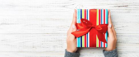 Woman arms holding gift box with colored ribbon on white rustic wooden table background, top view and copy space for you design photo