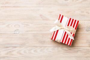 Beautiful gift box with a colored bow on the orange wooden table. Top view with copy space for you design. Christmas concept photo