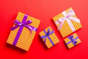 envuelto Navidad o otro fiesta hecho a mano presente en papel con púrpura y rosado cinta en rojo antecedentes. presente caja, decoración de regalo en de colores mesa, parte superior ver foto