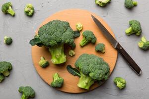 fresh green broccoli on wooden cutting board with knife. Broccoli cabbage leaves. light background. Flat lay photo