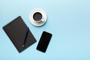 Modern office desk table with notebook, smartphone and other supplies with cup of coffee. Blank notebook page for you design. Top view, flat lay photo