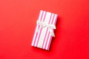 wrapped Christmas or other holiday handmade present in paper with white ribbon on red background. Present box, decoration of gift on colored table, top view with copy space photo