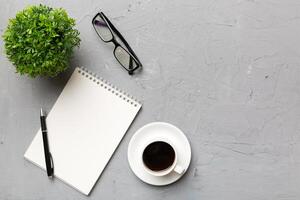 Modern office desk table with notebook and other supplies with cup of coffee. Blank notebook page for you design. Top view, flat lay photo