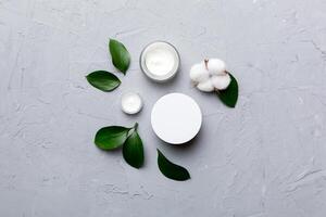 Organic cosmetic products with cotton flower and green leaves on cement background. Flat lay photo