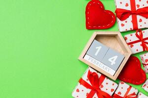 Holiday composition of gift boxes, wooden calendar and red textile hearts on colorful background with empty space for your design. The fourteenth of February. Top view of Valentine's Day concept photo