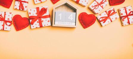 Top view of gift boxes, wooden calendar and red textile hearts on colorful background. The fourteenth of february. St Valentine's day concept with copy space photo