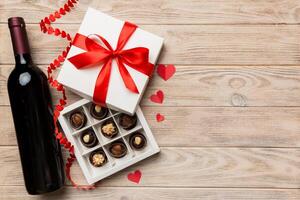 Bottle of red wine on colored background for Valentine Day with gift and chocolate. Heart shaped with gift box of chocolates top view with copy space photo