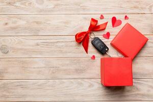 Black car key in a present box with a ribbon and red heart on colored background. Valentine day composition Top view photo