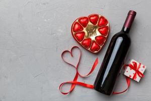 Bottle of red wine on colored background for Valentine Day with gift and chocolate. Heart shaped with gift box of chocolates top view with copy space photo