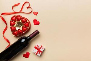 Bottle of red wine on colored background for Valentine Day with gift and chocolate. Heart shaped with gift box of chocolates top view with copy space photo