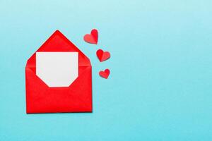 Red paper envelope with empty white card and heart on colored background. top view valentines day concept photo