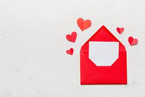 Red paper envelope with empty white card and heart on colored background. top view valentines day concept photo