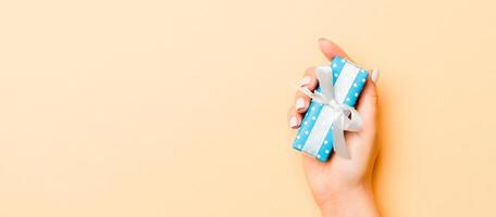 Flat lay of woman hands holding gift wrapped and decorated with bow on gold background with copy space. Christmas and holiday concept photo