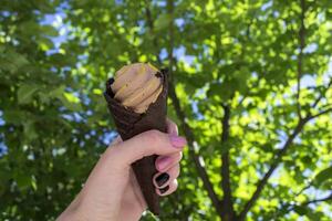 An ice cream cone in female arm against a green tree background photo