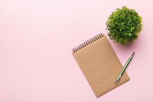 moderno oficina escritorio mesa con cuaderno y otro suministros con verde árbol. blanco cuaderno página para usted diseño. parte superior vista, plano laico foto