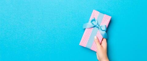 Woman arms holding gift box with colored ribbon on blue table background, top view and copy space for you design photo