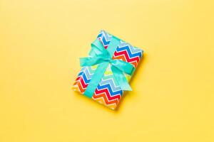 Gift box with blue bow for Christmas or New Year day on yellow background, top view with copy space photo