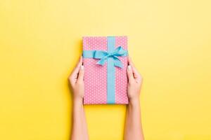 Woman arms holding gift box with colored ribbon on yellow table background, top view and copy space for you design photo