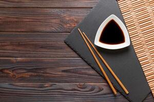 Chopsticks and soy sauce on black stone plate, wooden background with copy space photo