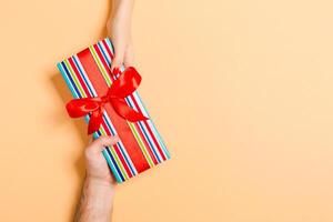 Top view of giving and receiving a present on colorful background. A man and a woman holding gift in hands. Festive concept with copy space photo