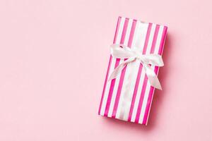 wrapped Christmas or other holiday handmade present in paper with white ribbon on pink background. Present box, decoration of gift on colored table, top view with copy space photo