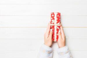 Female's hands holding striped gift box with colored ribbon on white rustic wooden background. Christmas concept or other holiday handmade present box, concept top view with copy space photo