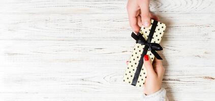 Top view of male and female hands holding present box on wooden background. Sharing a gift concept. Copy space photo