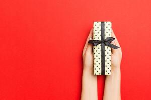 Female's hands holding striped gift box with colored ribbon on red background. Christmas concept or other holiday handmade present box, concept top view with copy space photo