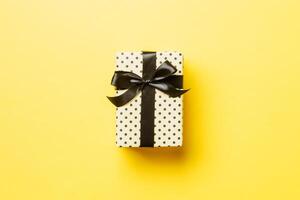 wrapped Christmas or other holiday handmade present in paper with black ribbon on yellow background. Present box, decoration of gift on colored table, top view with copy space photo