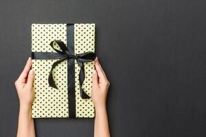 Top view of female hands holding christmas or other holiday handmade present box package in the palms, flat lay on black background with copy space photo