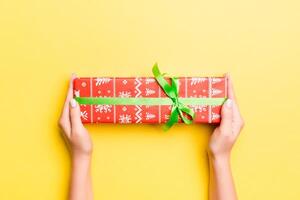 Woman arms holding gift box with colored ribbon on yellow table background, top view and copy space for you design photo