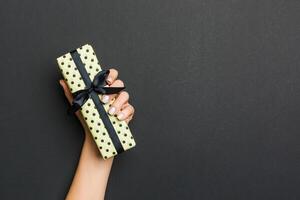 Top view of female hands holding christmas or other holiday handmade present box package in the palms, flat lay on black background with copy space photo