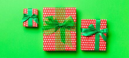 wrapped Christmas or other holiday handmade present in paper with green ribbon on green background. Present box, decoration of gift on colored table, top view photo