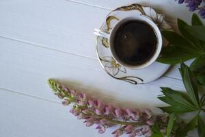 A cup of coffee and lupine flowers on a white wooden table. photo