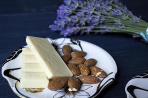 The white chocolate and almond nuts in the saucer and lavender on a blue table. photo