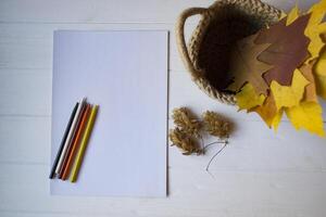 blanco papel, multicolor lapices y otoño hojas en un cesta en el escritorio. foto