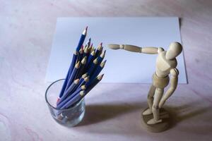 Colored pencils, empty paper and dummy for drawing on the table. photo